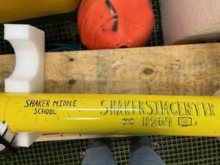 Yellow float lies in a crate with the word "Shaker Sim Center" written on it
