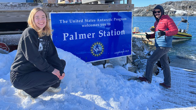 Josie Adams and Ben Freiberger during their quick visit to Palmer Station, crouching in front of the Palmer Station sign. Photo by Josie Adams