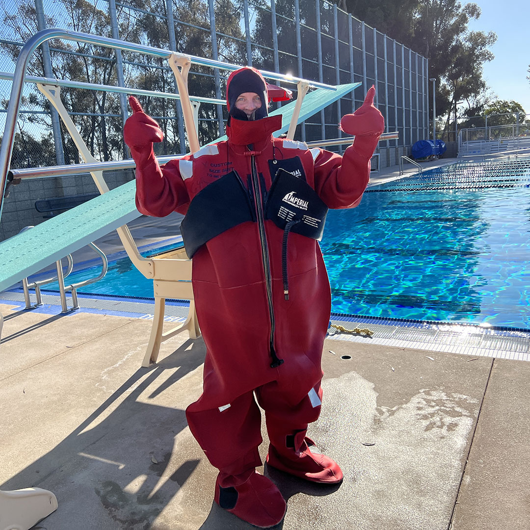 Person in a neoprene survival suit stands in front of a pool with two thumbs up