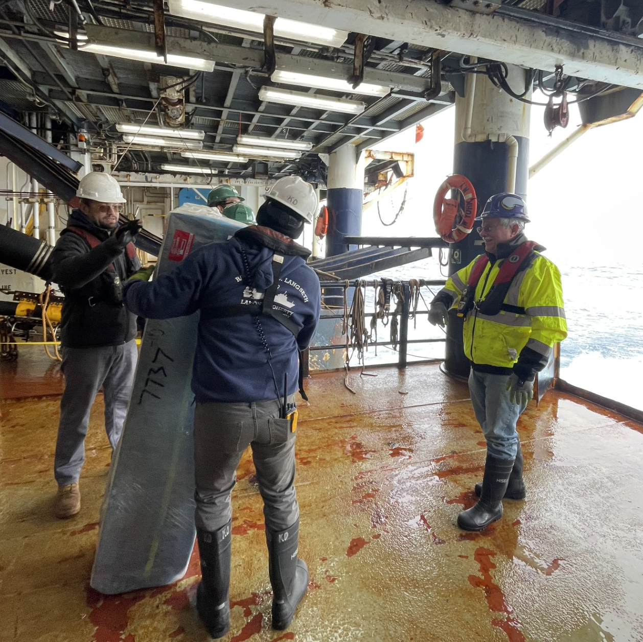 Koray Ergun, Lamont-Doherty Earth Observatory (LDEO) Marine Science Technician, Aaron Martin, and Todd Jensvold bring the Core Argo float to the stern of the Langseth.